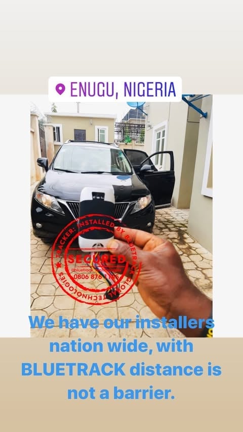 Hand holding a car key fob in front of a black SUV in Enugu, Nigeria, advertising Bluetrackgps installer services